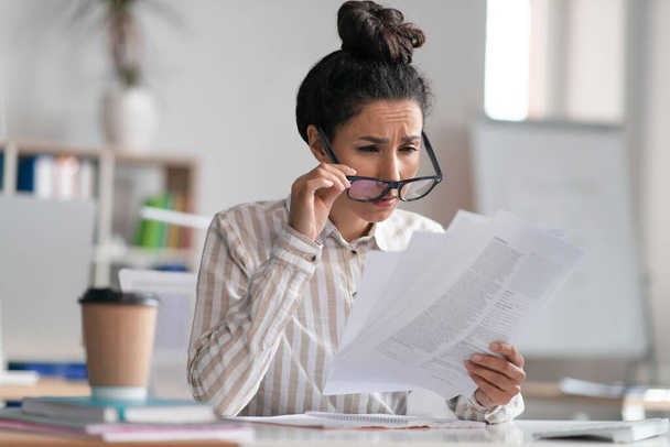 Gerente de escritório feminino vestindo óculos e fazendo papelada, tendo problemas de visão, sentado no local de trabalho - Foto, Imagem