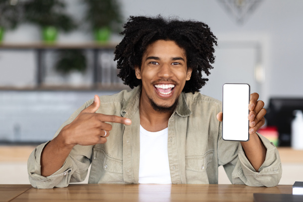 Froh happy millennial afrikanisch-amerikanischer Lockenkopf zeigt mit dem Finger auf Smartphone mit leerem Bildschirm - Foto, Bild