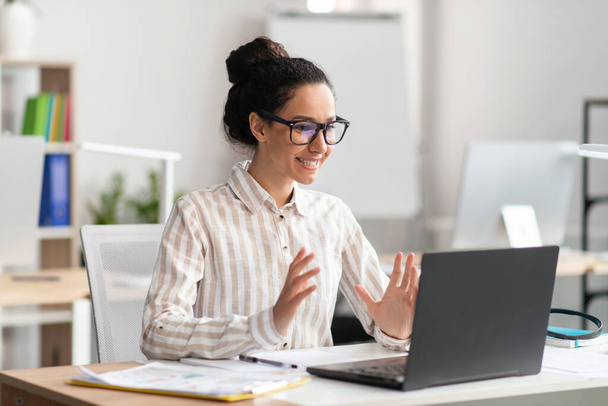 Atrakcyjna Latynoska kobieta mająca wideokonferencję z klientami lub partnerami biznesowymi, siedząca w biurze - Zdjęcie, obraz