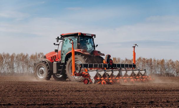 Spring sowing season. Farmer with a tractor sows corn seeds on his field. Planting corn with trailed planter. Farming seeding. The concept of agriculture and agricultural machinery. - Foto, Imagen