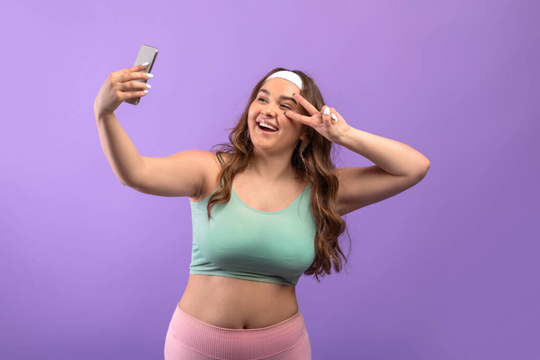 Alegre millennial europeo más tamaño dama en ropa deportiva tomar selfie en el teléfono y disparar transmisión en vivo - Foto, imagen