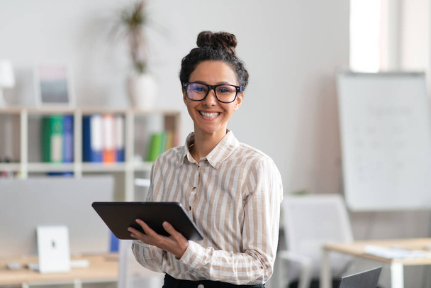 Щаслива підприємець молода жінка тримає цифровий планшет, використовуючи сучасні технології в бізнесі, офісному інтер'єрі
 - Фото, зображення