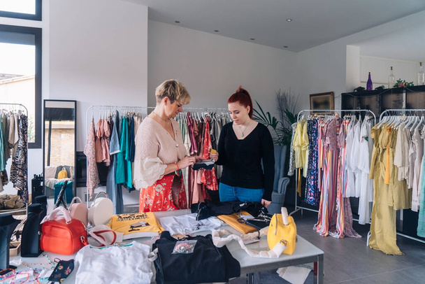 помощник продавца одежды консультирует клиента по поводу покупки. молодая женщина оплачивает одежду кредитной картой. - Фото, изображение