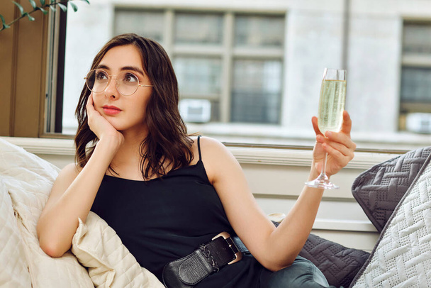 Bir kadeh şampanyayla kanepede dinlenen güzel genç bir kadın. - Fotoğraf, Görsel