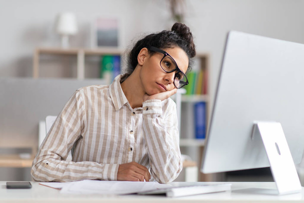 Portrait d'une femme d'affaires ennuyée assise au bureau, penchée la tête sur la main et regardant un écran d'ordinateur - Photo, image