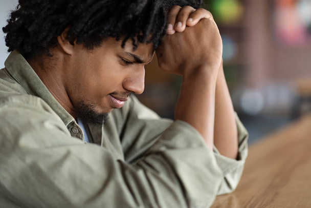 Sad serious concentrated young african american curly male praying or thinking about solving problem - 写真・画像