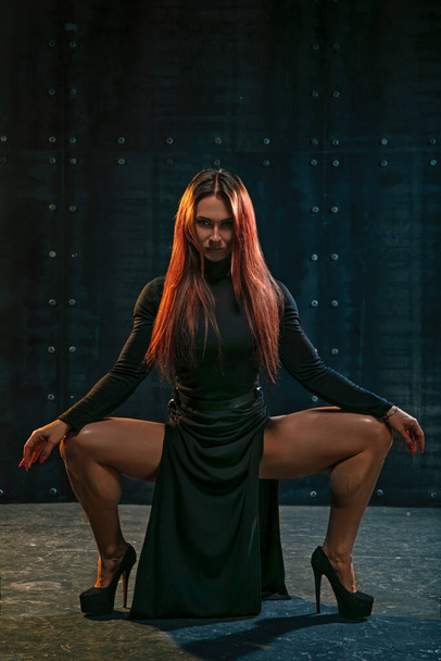 Attractive red-haired girl in black dress demonstrates athletic legs - Photo, Image