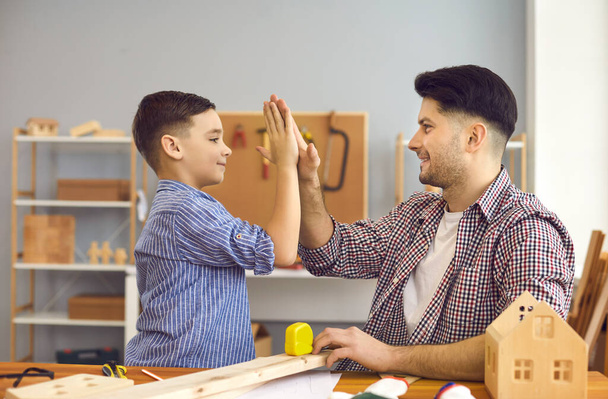 Happy smiling father giving high five and support to son at home workshop - Фото, изображение