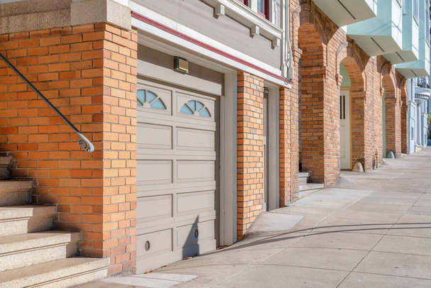 Роща игрушечных домов с лестничными маршами и гаражом на фасаде в Сан-Франциско, Калифорния. Снаружи таунхаус с апельсиновым кирпичом и коричневой дверью гаража с оконной панелью. - Фото, изображение