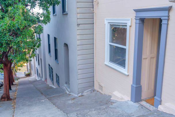 Strome zbocze betonowego chodnika bocznego ze schodami w środku w San Francisco, Kalifornia. Po prawej stronie znajdują się budynki mieszkalne w poprzek drzew po lewej stronie i widok na drogę z tyłu. - Zdjęcie, obraz