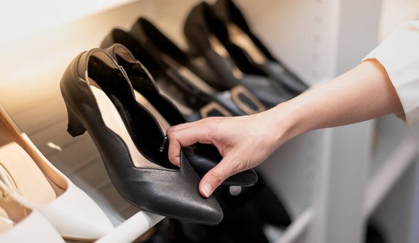 Žena držící boty v rukou vybírat a nakupovat při pohledu na police s četnými obuví. - Fotografie, Obrázek