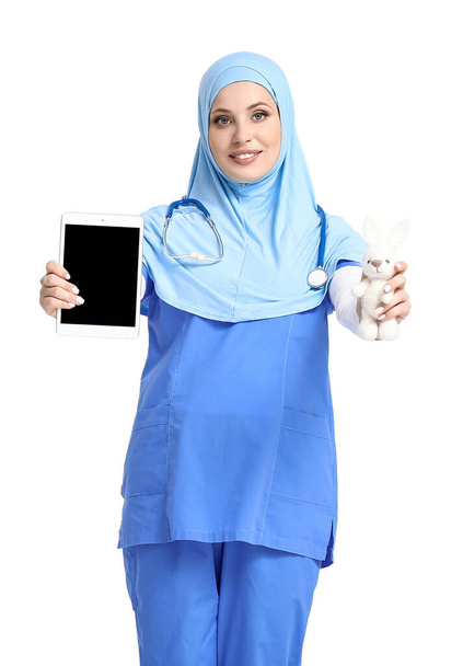 Muslim pediatrician with toy and tablet computer on light background - Foto, imagen