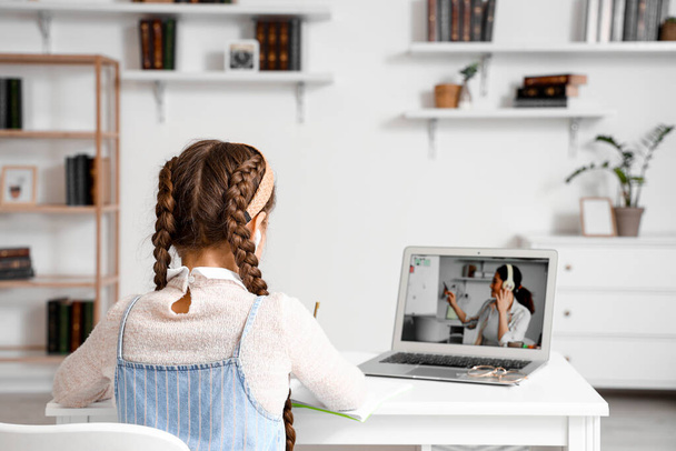 Девочка в наушниках учится с онлайн репетитором дома, вид сзади - Фото, изображение