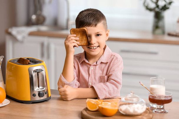 Cute little boy with toasted bread slice in kitchen - Фото, изображение