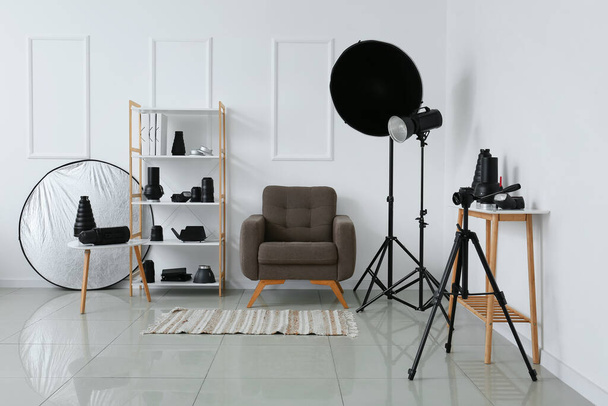 Sisätilojen valokuvastudio nojatuoli, hylly yksikkö ja erilaiset modernit laitteet lähellä valoseinää - Valokuva, kuva