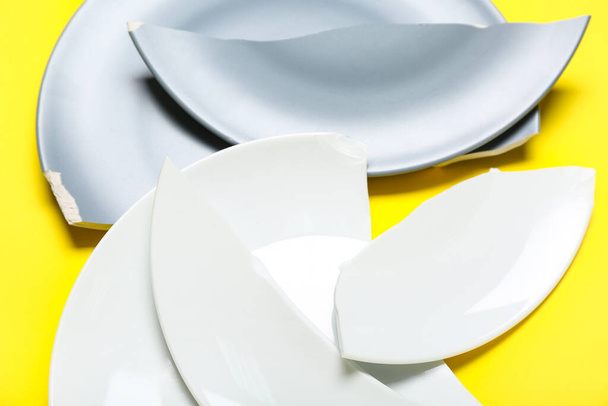 Broken ceramic plates on yellow background, closeup - 写真・画像