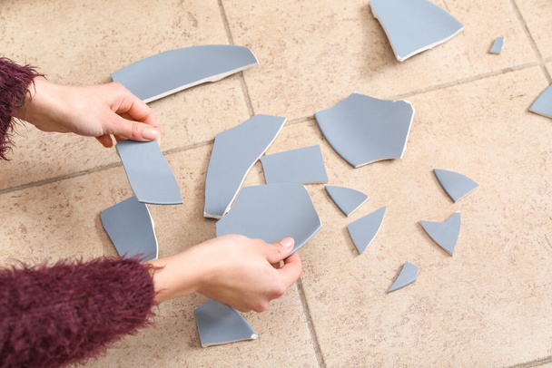 Жіночі руки з розбитою керамічною пластиною на кольоровій плитці
 - Фото, зображення