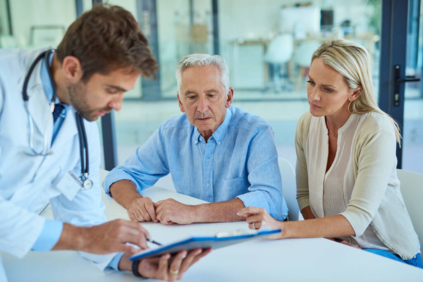 Lets take a closer look at your test results. Shot of a doctor discussing some paperwork with a senior patient and his daughter in a clinic. - Foto, immagini