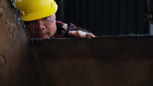 Mannelijke werknemer met een bril en bouwhandschoenen inspecteert het werk na het slijpen van metaal met een haakse slijper in de werkplaats. - Video