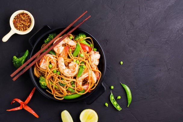 Míchané špagety nebo smažené nudle se zeleninou a krevetami v černé misce. tmavé pozadí, horní pohled - Fotografie, Obrázek