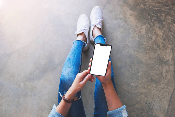 Top view mockup image of a woman holding black mobile phone with blank white screen while sitting on the floor - Фото, зображення