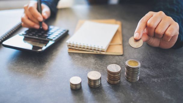 Imprenditrice che detiene e impila monete mentre calcola i soldi sul tavolo - Foto, immagini