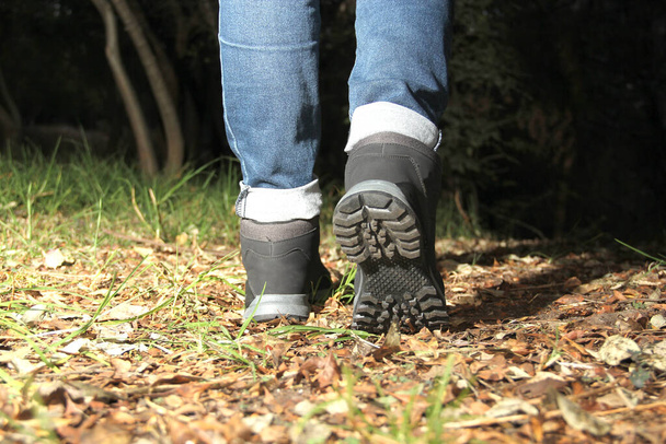Legs of a woman with denim pants and black hiking boots walking alone in the forest as part of the social problem of disappearances and unlocated victims of kidnapping, rape, femicide in the dark - Fotoğraf, Görsel