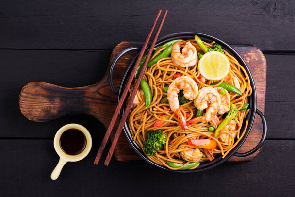 Míchané špagety nebo smažené nudle se zeleninou a krevetami v černé misce. tmavé pozadí, horní pohled - Fotografie, Obrázek