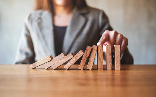 Closeup image of a businesswoman's finger try to stopping falling wooden dominoes blocks for business solution concept  - 写真・画像