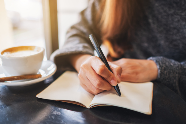 Szoros kép egy nőről, aki egy üres jegyzetfüzetre ír az asztalon.  - Fotó, kép