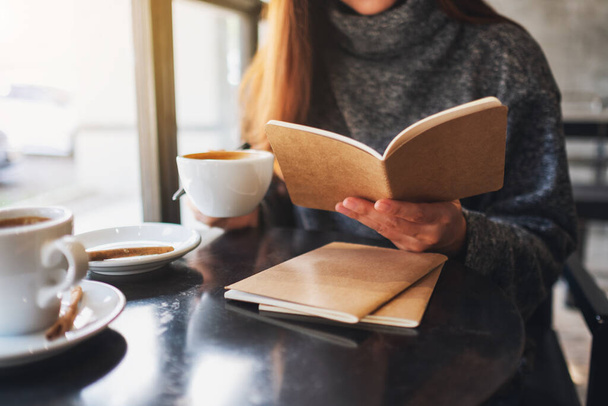 Κοντινή εικόνα μιας γυναίκας που διαβάζει ένα βιβλίο πίνοντας καφέ στο cafe  - Φωτογραφία, εικόνα