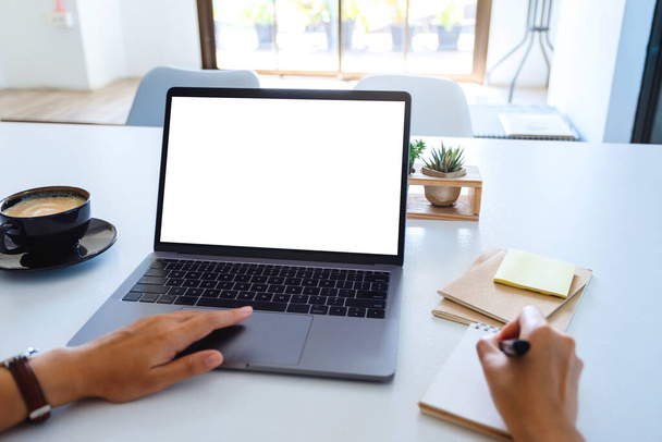 Mockup-Bild einer Frau, die ein Laptop-Touchpad mit leerem weißen Desktop-Bildschirm benutzt und berührt, während sie auf einem Notebook schreibt - Foto, Bild