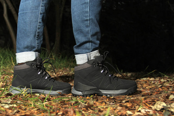 Legs of a woman with denim pants and black hiking boots walking alone in the forest as part of the social problem of disappearances and unlocated victims of kidnapping, rape, femicide in the dark - Φωτογραφία, εικόνα