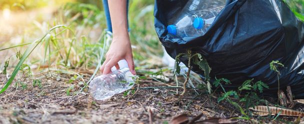 Closeup image of a woman picking up garbage plastic bottles into a bag for recycling concept - Foto, Imagen
