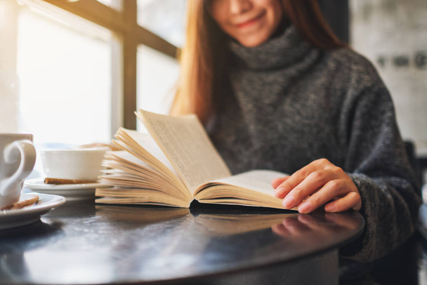 Close-up afbeelding van een mooie vrouw die een boek met koffiebeker op tafel vasthoudt en leest - Foto, afbeelding