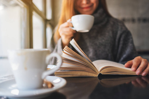 Κοντινό πλάνο εικόνα μιας όμορφης γυναίκας που διαβάζει ένα βιβλίο ενώ πίνει καφέ το πρωί - Φωτογραφία, εικόνα