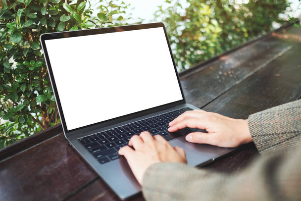 Εικόνα mockup μιας γυναίκας που χρησιμοποιεί και πληκτρολογεί σε φορητό υπολογιστή με λευκή οθόνη επιφάνειας εργασίας στην ύπαιθρο - Φωτογραφία, εικόνα