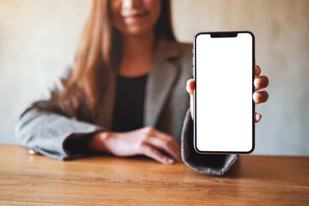 Imagen burlona de una mujer de negocios asiática sosteniendo y mostrando el teléfono móvil negro con pantalla blanca en blanco en la cafetería - Foto, imagen