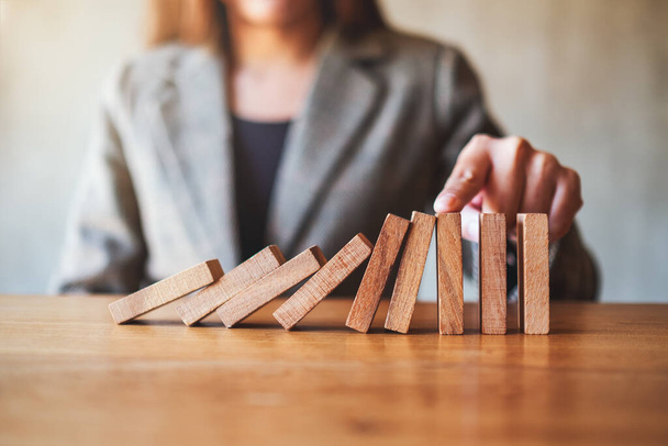 Immagine ravvicinata del dito di una donna d'affari tenta di smettere di cadere blocchi di domino in legno per concetto di soluzione aziendale  - Foto, immagini