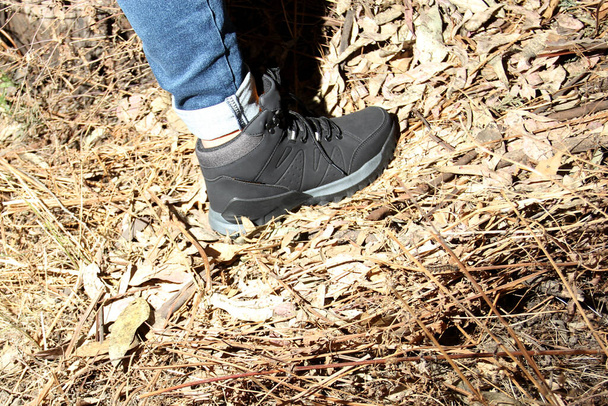 Legs of a woman with denim pants and black hiking boots walking alone in the forest as part of the social problem of disappearances and unlocated victims of kidnapping, rape, femicide in the dark - Foto, Bild