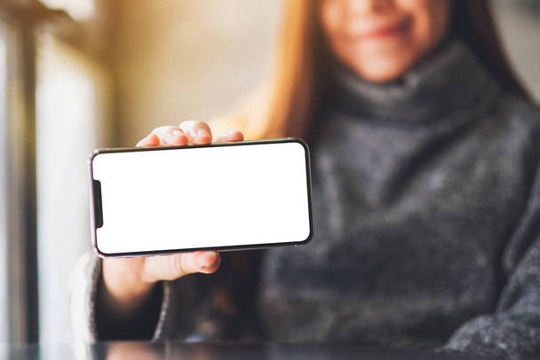 Mockup-Bild einer asiatischen Frau, die ein schwarzes Handy mit leerem weißen Bildschirm hält und zeigt  - Foto, Bild