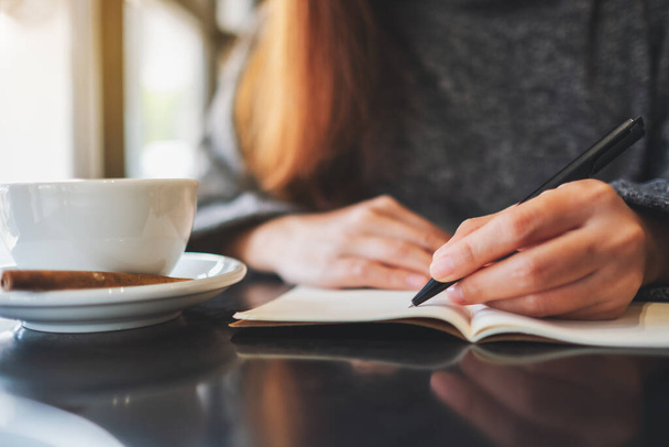 Immagine ravvicinata di una donna che scrive su un quaderno bianco sul tavolo  - Foto, immagini
