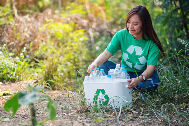 Красива азіатська жінка, що збирає сміття пластикові пляшки в кошик на відкритому повітрі
 - Фото, зображення