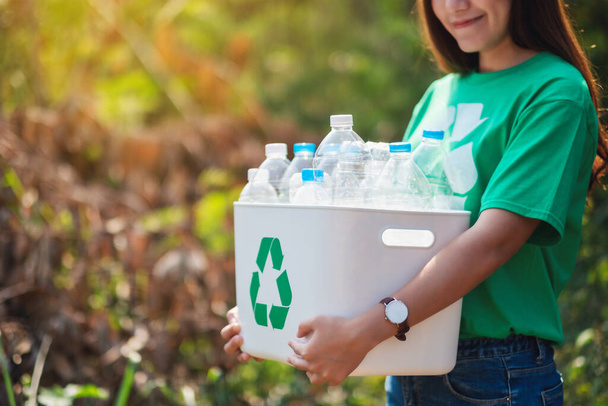 Una hermosa mujer asiática recogiendo basura y sosteniendo una papelera de reciclaje con botellas de plástico al aire libre - Foto, imagen