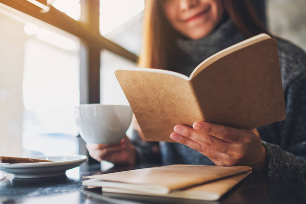 Nahaufnahme einer schönen Frau, die morgens beim Kaffeetrinken ein Buch liest - Foto, Bild