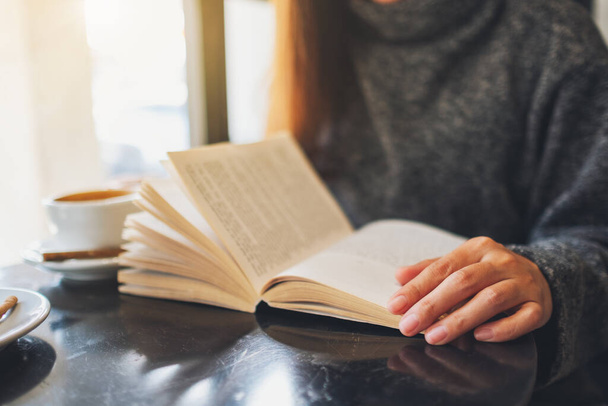 Immagine ravvicinata di una bella donna che tiene in mano e legge un libro con una tazza di caffè sul tavolo - Foto, immagini