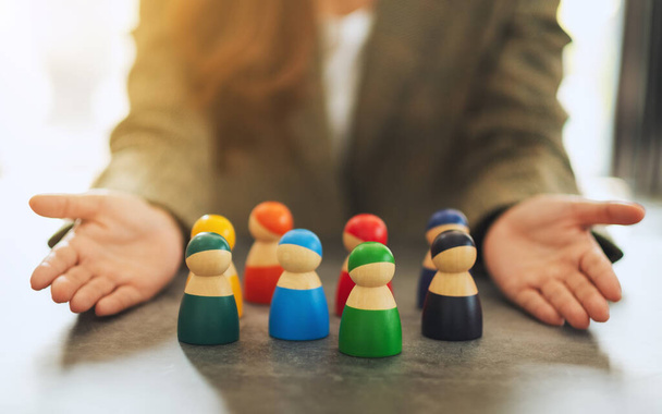 Closeup image of a woman showing a group of different colors wooden people toy in hands for diversity and business concept - Photo, Image