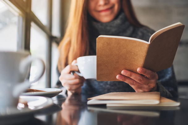 close-up beeld van een mooie aziatische vrouw het lezen van een boek tijdens het drinken van koffie in cafe  - Foto, afbeelding