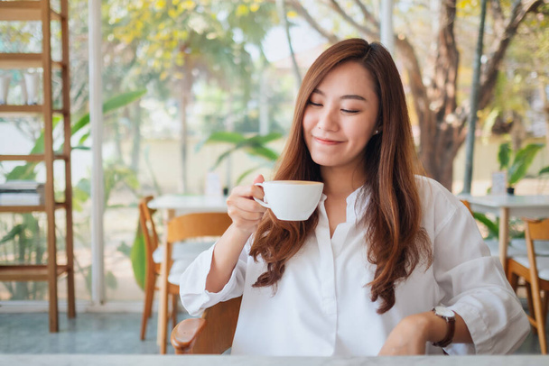 Closeup image of a beautiful asian woman holding and drinking hot coffee with feeling good in cafe - Photo, Image