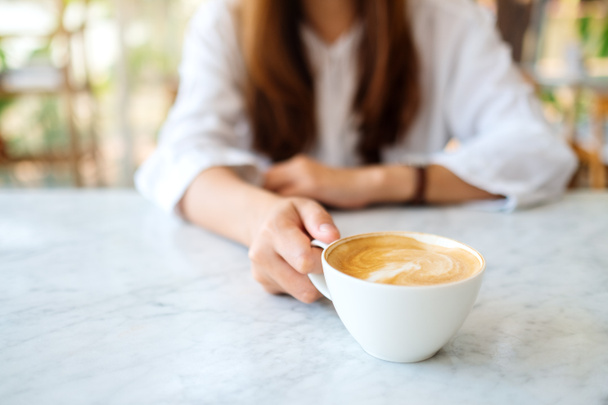 Masanın üzerinde bir fincan sıcak kahve tutan bir kadının yakın plan görüntüsü. - Fotoğraf, Görsel
